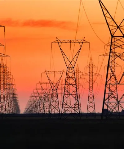Series of high-voltage power transmission towers carrying electricity across a wide service corridor.