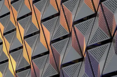Bild einer grauen Metallverkleidung an einem Gebäude mit Löchern, die ein interessantes Muster aus Licht und Schatten in dreieckigen Formen bilden