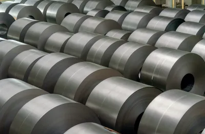 A large number of rolled steel coils stacked in rows inside an industrial warehouse.