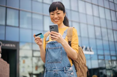 young woman looking at phone with credit card in other hand
