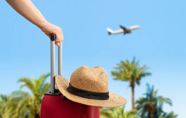 suitcase with sunhat and plane flying in the background