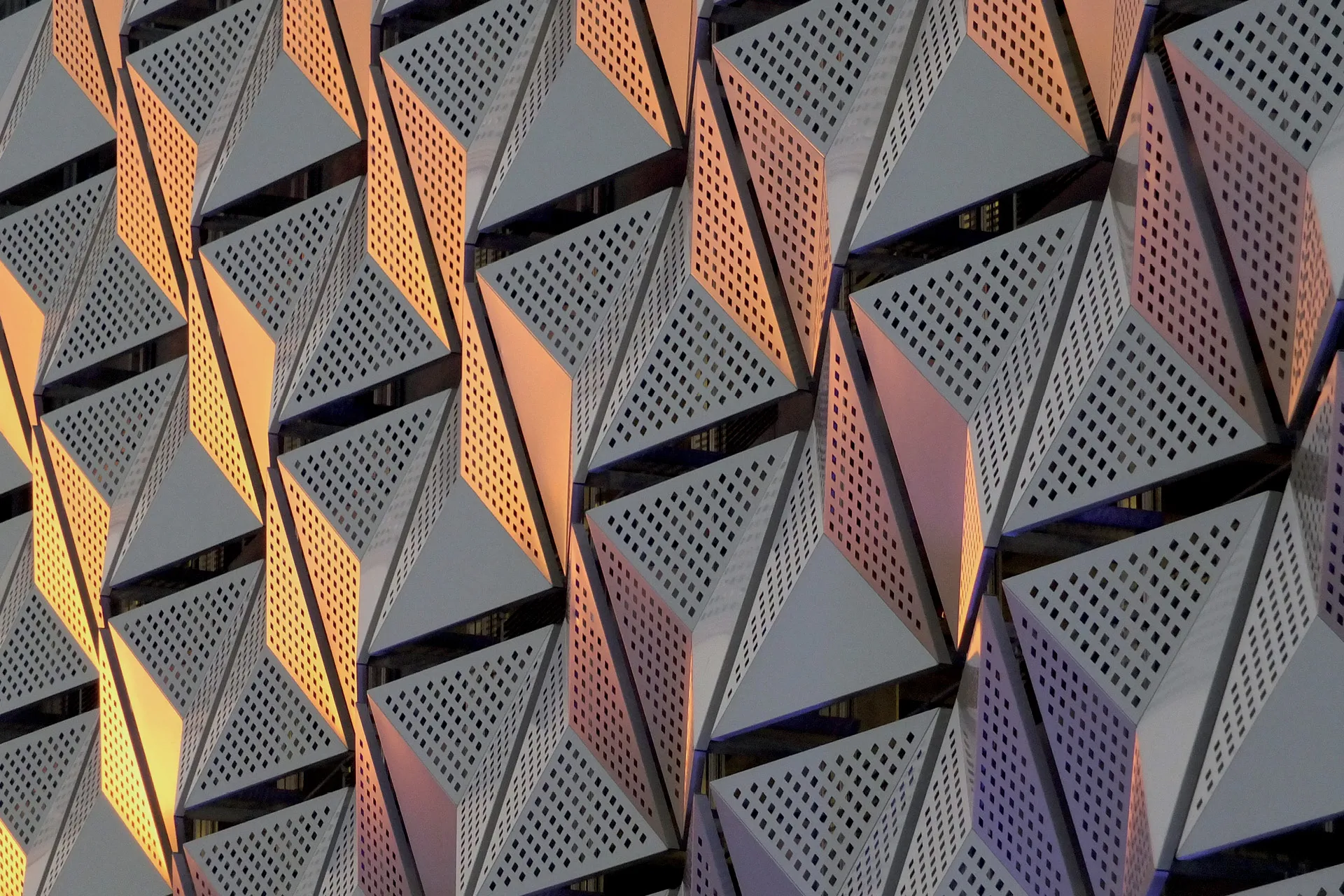 Bild einer grauen Metallverkleidung an einem Gebäude mit Löchern, die ein interessantes Muster aus Licht und Schatten in dreieckigen Formen bilden