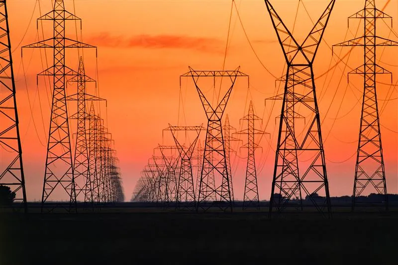 Series of high-voltage power transmission towers carrying electricity across a wide service corridor.
